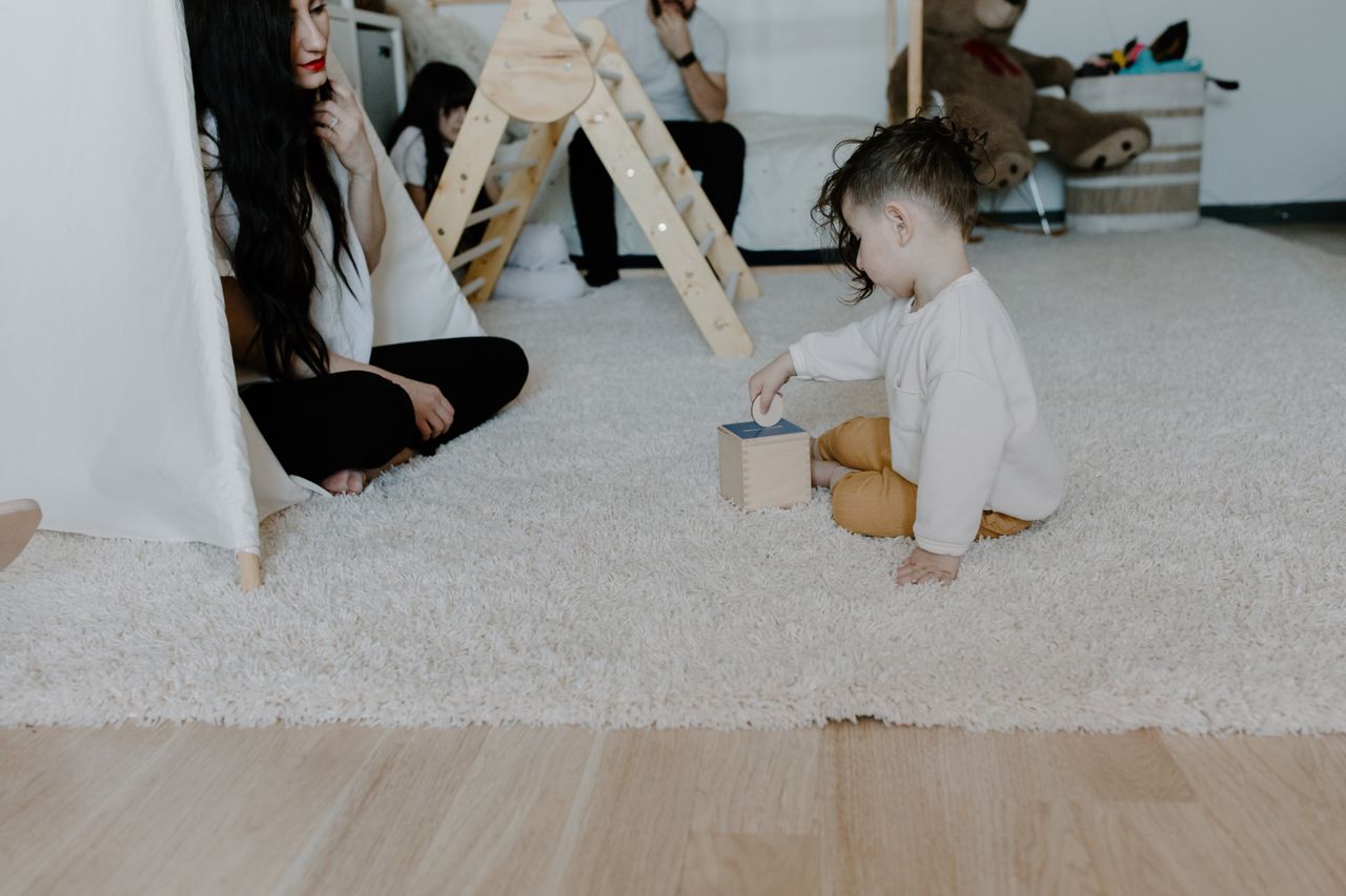 A mother and child enjoying playtime on a carpeted floor with toys.